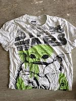 White Star Wars T-shirt with large distressed black STAR WARS text and green Grogu graphic on front lying flat on a rustic wooden surface.