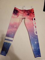 Full view of the leggings laid flat showing galaxy print, white stripes near ankles, and large AIM'N logo on side.