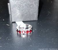 Ring shown on a black surface with box partially open behind it.