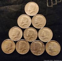 Obverse view of ten Kennedy half dollars arranged in pyramid, showing bust of JFK and visible dates.
