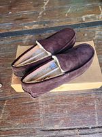 Pair of brown suede UGG men's slippers, size 10, placed on a wooden surface with visible soft lining inside.