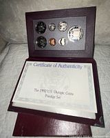 Open burgundy presentation case showing seven proof coins and certificate of authenticity