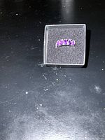 Photo of silver-tone ring with five tear drop shaped amethyst stones arranged in a row inside a small black jewelry box on a black surface.