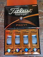 Top view showing one large unopened black and orange box labeled Titleist Pro V1, with four smaller unopened orange boxes containing golf balls in front.