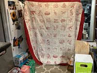 Full view of antique embroidered quilt showing cream fabric with red embroidered squares and a solid red border, displayed hanging.