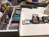 Magic: The Gathering trading cards in white box with assorted colored card sleeves separated by color.