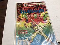 Photo of Charlton Bullseye comic book issue #11 with cover showing Captain Atom and green-skinned character, encased in plastic sleeve.