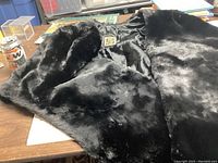 Black fur stole laid on a wooden table showing the plush fur exterior and partial satin lining.