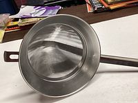Top-down view of a stainless steel conical food chinois strainer with a holding tab.