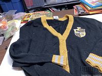 Black Hufflepuff sweater with yellow trim laid flat showing full front buttons and left sleeve cuff detailing