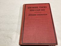 Front cover of red hardbound magic book with printed title and author name.