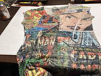 Photo of a large-sized T-shirt displaying a colorful print of vintage Marvel comic book covers and characters on a table.