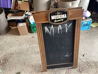 Full front view of wooden clapboard style chalkboard sign with Muskoka Brewery logo plaque at top. Chalk markings visible on board.