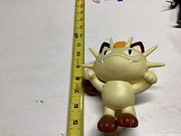 Photo of the Meowth figure next to a measuring tape showing its height about 7 inches tall.