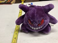 Purple Gengar plush toy on a white background with a measuring tape showing approximately 8-inch width.