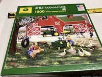 Puzzle box showing artwork for 1000 piece John Deere 'Little Farmhands' jigsaw puzzle depicting a vibrant farm scene with children, animals, and a barn.