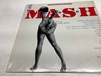 Front cover of M*A*S*H vinyl record showing the iconic peace sign hand with legs and red "M*A*S*H" text against a white background.