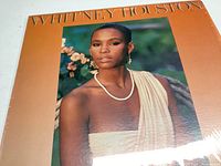 Front cover of the Whitney Houston vinyl LP showing a portrait of Whitney Houston wearing a pearl necklace and cream one-shoulder garment.