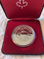 Close-up image of the 1979 Canadian silver dollar coin with detailed Griffon ship design inside red velvet-lined box with maple leaf embroidery