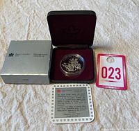 1990 Canadian Silver Dollar Proof Coin displayed inside hinged burgundy velvet case and silver outer box, along with certificate of authenticity and auction lot tag.