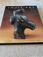 Front cover of the book showing the artwork of a black stone Inuit sculpture on a brown to black gradient background with the title 'INUIT ART' and author and photographer names at the bottom.