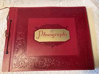 Top view of vintage red leather photo album with embossed floral design and gold label 'Photographs' on front cover.