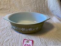 Single vintage Pyrex ovenware bowl with Crazy Daisy white floral pattern on avocado green background, shown from top angle to reveal interior and exterior.