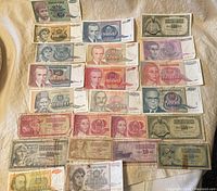 Overview of 25 Yugoslavian banknotes laid out on fabric showing various portraits and denominations