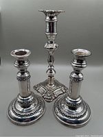 Photo shows a pair of 19th century silver plate telescoping candlesticks and one single tall antique silver plate candlestick, all with ornate detailing and round bases.