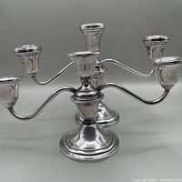 Pair of two unmatched sterling silver candelabra arranged side by side showing their design and dents.