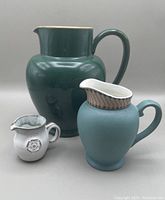 Three ceramic pitchers of different sizes arranged together showing front views.