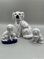 Photo showing all three porcelain dog figurines: one large seated dog, a group of three smaller dogs on a blue base, and a single smaller dog holding a basket