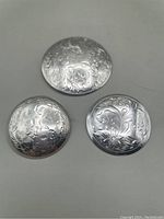 Three round vintage sterling silver brooches with detailed engraving laid flat against gray background