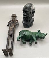 Photo showing all three items together: hand-carved bust, green stone rhinoceros, and metal warrior figure.