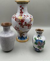 Three cloisonné vases together showing sizes and varied floral patterns on white backgrounds.