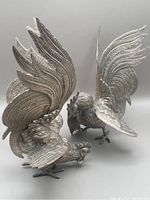 Two brass fighting rooster figurines showing detailed engravings, raised wings, and visible brass solder seams.
