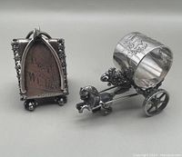 Photo of two antique Meriden quadruple silver plate napkin rings; one triangular engraved with 'Best Wishes' and monogram; the other a horse pulling a carriage figural ring.