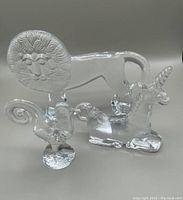 Three clear glass animal figures (lion, unicorn, rooster) together showing their profile and flat backs.