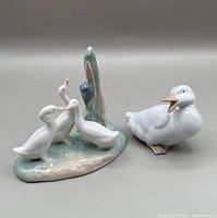 Group of three white ducklings on a green/beige base next to single white duck with open beak