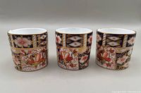 Front view of three square-shaped Royal Crown Derby Imari demitasse cups showing intricate multicolor floral and geometric designs.