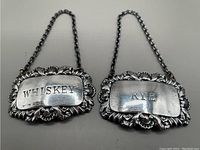 Pair of sterling silver Whiskey and Rye decanter tags with chains and detailed floral designs.