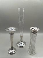 Three vases side by side: tall etched glass vase, cut crystal vase with beaded sterling rim, and Birks sterling silver vase with wide rim.