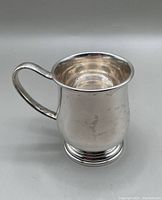 Front side view of sterling silver child’s mug showing handle and body shape.