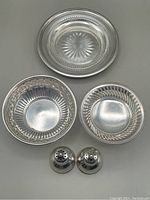 Top view grouping of sterling silver items including pierced bowls, small pedestal bowl, butter dish with glass liner, and Birks salt and pepper shakers.