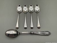 Four sterling silver teaspoons and one sterling handled tea infuser laid flat on gray background