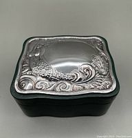 Closed green leather box with an ornate sterling silver top featuring a mermaid design in raised relief.