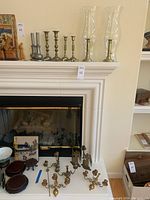 Shelf display showing pewter and brass candlesticks, wall-mounted candleholders, and glass hurricane candle covers