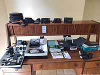 Multiple cameras, lenses and accessories arranged on wooden cabinet shelves
