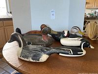 Seven vintage wooden duck decoys arranged on a wooden table showing varied paint styles and conditions.