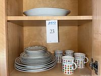 Stack of plates, bowls, and cups with colorful floral design inside a wooden cabinet.